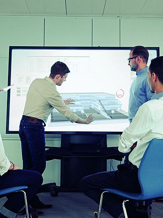 Menschen sitzend und stehend betrachten einen digitalen Bauplan auf einem Bildschirm