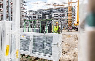 Man in yellow vest on a forklift truck with glass windows. Construction site with yellow crane in the background