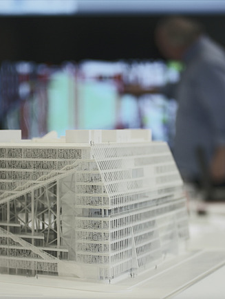 Model of a building in the foreground with people and canvas in the background