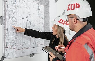 View of a plan in front of which two people with construction helmets are standing and talking about it